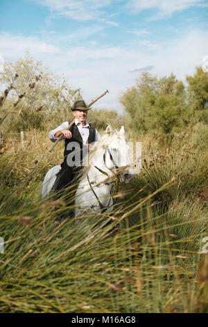 Gardian o tradizionali bull herder in tipici abiti da lavoro al galoppo su un cavallo Camargue, Le Grau-du-Roi, Camargue, Francia Foto Stock