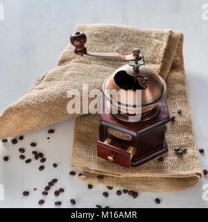 Vecchio macinino da caffè sul sacco di iuta, i chicchi di caffè sulla terra bianca Foto Stock