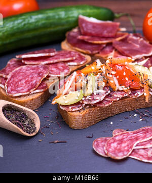 Un panino con salsiccia affumicata salumi e verdura spruzzata con sesamo e basilico essiccato su sfondo nero Foto Stock