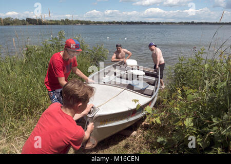 I membri della famiglia tirando alluminio barche da pesca sulla riva attraverso intonso impollinatrice erbacce lungo il litorale dal lago Clitherall Minnesota MN USA Foto Stock