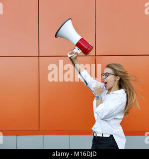 Una giovane ragazza attraente in una camicia bianca e occhiali è in possesso di un altoparlante nelle sue mani. Lei urla al megafono. Protesta. Lotta per righ Foto Stock