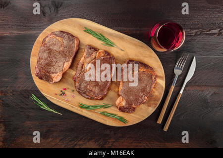 Una foto aerea di tre fette di carne cotta, filetti di manzo, ripresa dall'alto sul buio rustica con rametti di rosmarino, sale, pepe, vino, Foto Stock