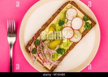 Vegetariano Avocado e formaggio con Ravanelli e cetriolini pane di segale aperto di fronte a Sandwich contro un sfondo rosa Foto Stock