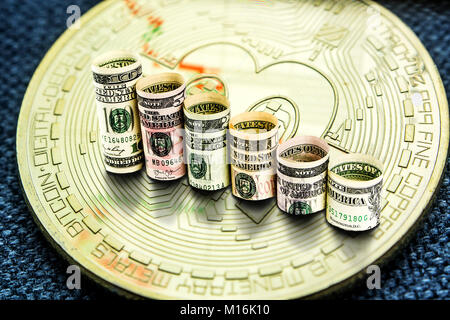 Primo piano della golden bitcoin moneta con un grafico la riflessione sulla sua superficie con il verde e le barre rosse e rotoli di banconote di dollari la formazione di fasi in declino Foto Stock