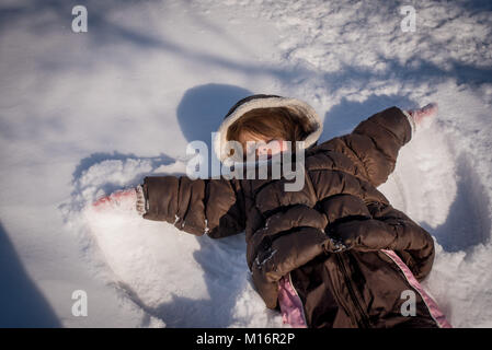 Una tre-anno vecchia ragazza fa un angelo di neve nella neve nel nordest degli Stati Uniti. Foto Stock