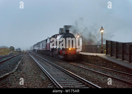 Stazione Ribblehead, 27 gennaio 2018. North Yorkshire. La prima locomotiva a vapore speciale del 2018 sull'Settle-Carlisle linea ferroviaria con locomotiva "Galatea' tira l'inverno montagna pennini Express, 27 gennaio. Tenebre cade su un nebbioso giorno come il treno passa attraverso la stazione. Credito: John Bentley/Alamy Live News Foto Stock