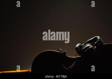 Silhouette di violoncello e cuffie sul buio, sfondo caldo Foto Stock