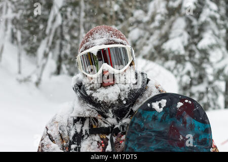 Ritratto di uomo barbuto occhiali da sci snowboard di contenimento in montagna. Foto Stock