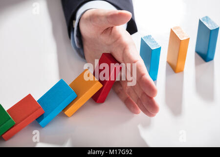 Elevato angolo di visione di un imprenditore colorato di arresto di domino di cadere sulla scrivania Foto Stock