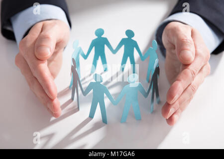 Close-up di un imprenditore la mano la protezione di carta blu tagliare le figure su sfondo bianco Foto Stock
