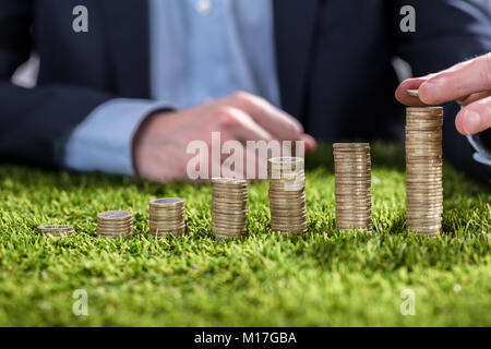 Close-up di un imprenditore la mano di monete di impilamento su erba verde Foto Stock