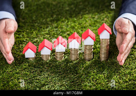 Vista in elevazione di un imprenditore la mano la protezione di modelli della casa su monete impilate su erba verde Foto Stock