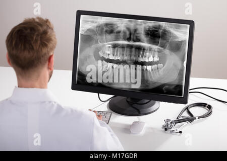 Vista posteriore di un medico di sesso maschile guardando a raggi X sul computer Foto Stock