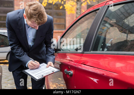 Agente di assicurazione iscritto sulla Clipboard mentre esaminando AUTO DOPO INCIDENTE Foto Stock