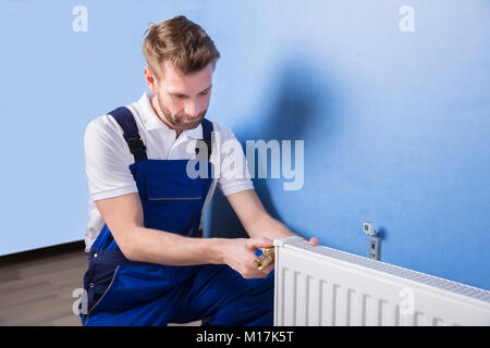 Giovane Maschio Idraulico In uniforme di installazione del radiatore Foto Stock
