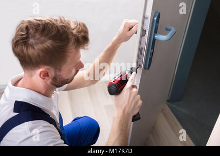 Giovane falegname Installazione del dispositivo di bloccaggio della porta con un cacciavite senza fili Foto Stock
