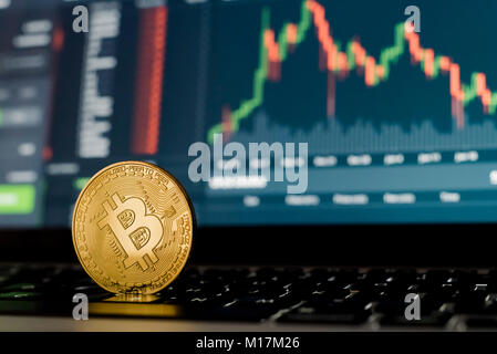 Coniate Bitcoin token cryptocurrency coin laterale ad angolo stretto fino in piedi sul lato sulla tastiera del computer con schermo di trading in background. Foto Stock