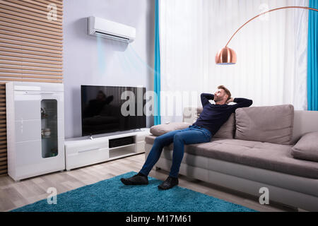 Giovane uomo rilassante sul divano vicino la televisione a casa Foto Stock