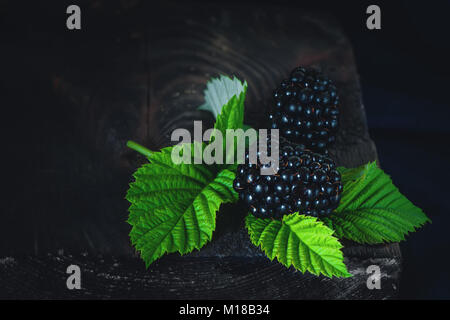 Mature shiny BlackBerry giacente su foglie su un tavolo di legno. Stile rustico. Copia dello spazio. Foto Stock