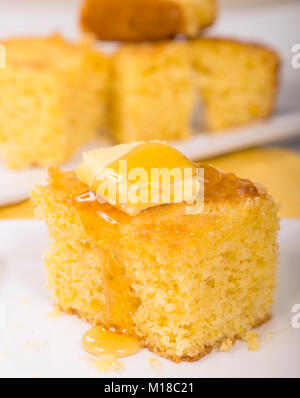 Pezzo di pane appena sfornato cornbread con burro e miele gocciolare fuori dalla parte superiore Foto Stock