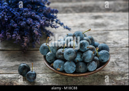 Autumn harvest blue prugnoli su un tavolo di legno con un bouquet di fiori di lavanda in background. Copia dello spazio. Stile rustico. Foto Stock