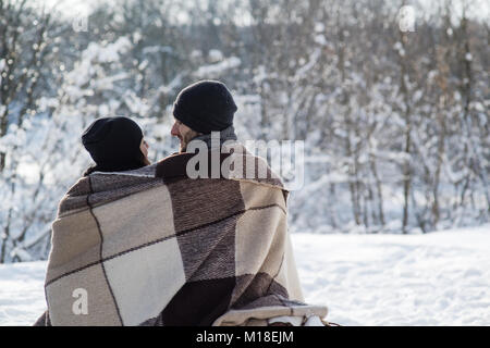 Un ragazzo e una ragazza in black hats e plaid seduti sulla neve sullo sfondo. L uomo e la donna di fronte all'altra. Foto Stock