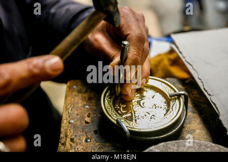 Un artigiano al lavoro su un pezzo di metallo dorato, in un tradizionale artwork e negozio di souvenir a Tunisi, Tunisia. Foto Stock