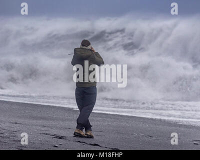 Tourist contro la tempesta le onde a Reynisfjara spiaggia di sabbia nera,Vik,Suðurland,Islanda Foto Stock