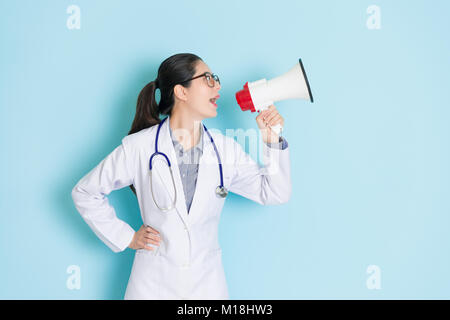 Felice bellissima femmina medico tramite altoparlante faccia a area vuota di parlare e di annunciare informazioni mediche isolato su sfondo blu. Foto Stock