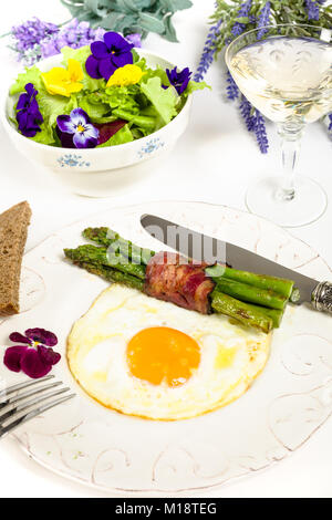 Uova con asparagi e pancetta affumicata su uno stile Mediterraneo servite con lattuga e fiori commestibili Foto Stock