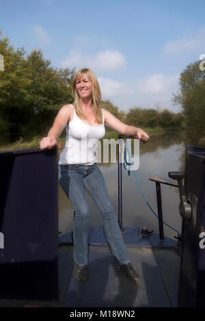 Donna che utilizza il timone per sterzare una narrowboat lungo un canale nel Regno Unito Foto Stock