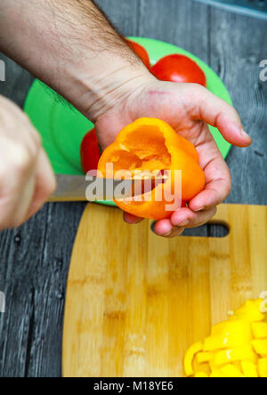 Mani maschio rimuovere i semi dai peperoni. Sul tavolo sono le verdure. Foto Stock