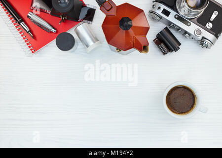 Vintage fotocamera con rotoli di pellicola, il blocco note e penna e red POT del caffè con la tazza di caffè in bianco sullo sfondo di legno vista piana Foto Stock