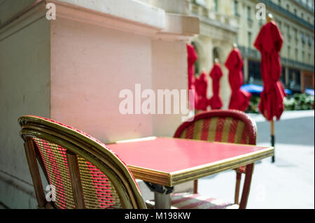 Tipica tabella e sedie di rattan sulla terrazza di un parigino outdoor cafe nella luce del sole con ombrelloni in background. Foto Stock