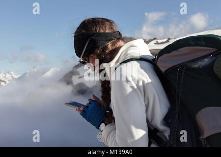 Una donna con un telefono cellulare in montagna su un percorso turistico comunica con gli amici tramite una connessione digitale in una rete sociale. Il concep Foto Stock