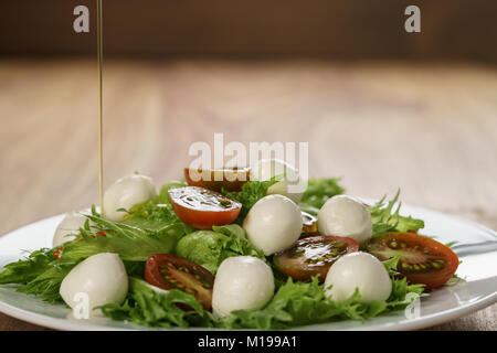 Versando l'olio d'oliva su insalata caprese con variazione kumato pomodori e foglie frillies Foto Stock