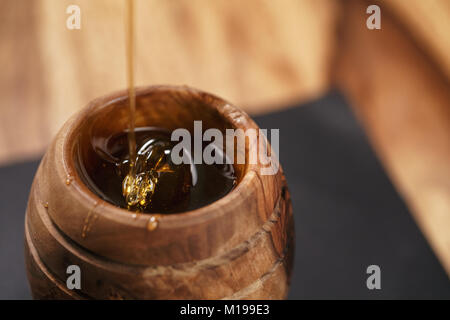 Miele biologico gocciola dal bilanciere di legno in vaso Foto Stock