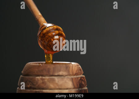 Miele biologico gocciola dal bilanciere di legno in vaso Foto Stock