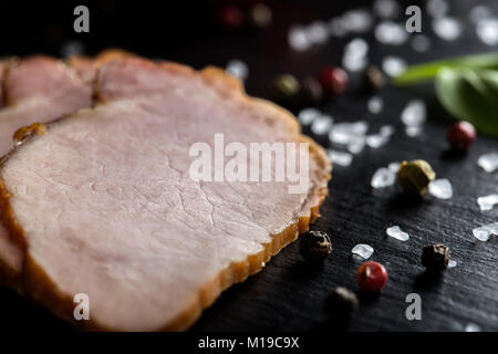 Dettaglio di un tradizionale delle fette di carne di maiale affumicata su ardesia scura con spezie Foto Stock