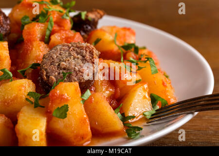 Patate in umido con le salsicce di maiale sulla piastra con forca Foto Stock