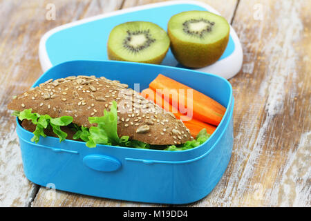 Un sano pranzo al sacco box contenente formaggio marrone sandwich, croccante di carote e kiwi Foto Stock