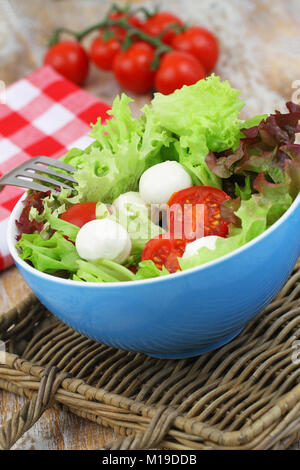 Sana insalata di mozzarella con pomodorini in blu ciotola sul vassoio di vimini Foto Stock