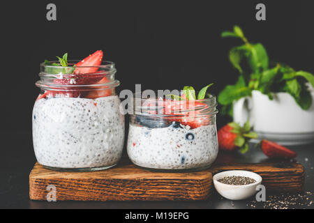 Chia pudding con fragole fresche e mirtilli decorato con foglia di menta su sfondo scuro. Copia spazio per il testo. Concetto di mangiare sano, dieta Foto Stock