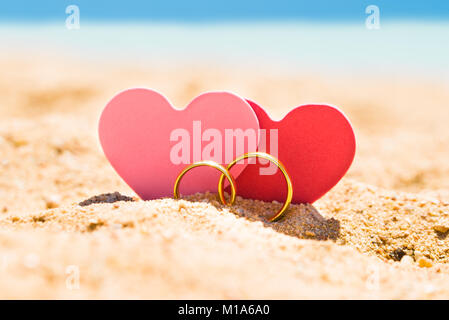 Due forme di cuore con anelli d oro sulla sabbia in spiaggia in estate Foto Stock