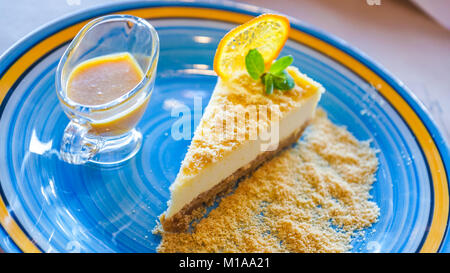 Cheesecake con mare-frangola salsa in una blu con striscia gialla piastra close up Foto Stock