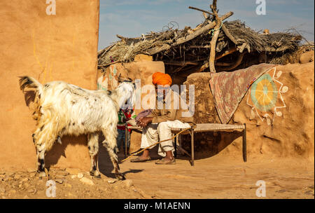 Vecchio tribale di Rajasthani uomo seduto su una branda in un villaggio rurale vicino al deserto di Thar Jaisalmer, Rajasthan. Foto Stock
