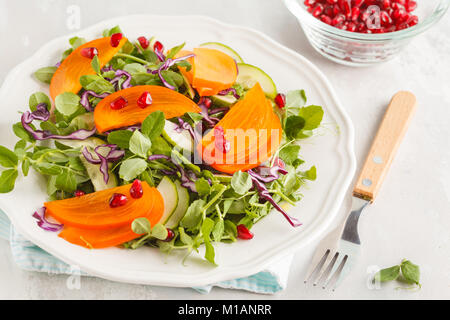 Persimmon insalata con foglie di piselli e melograno. Una sana alimentazione vegetariana concetto. Foto Stock