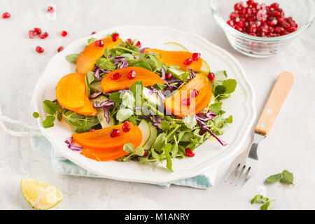 Persimmon insalata con foglie di piselli e melograno. Una sana alimentazione vegetariana concetto. Foto Stock