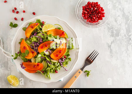 Persimmon insalata con foglie di piselli e melograno. Una sana alimentazione vegetariana concetto. Foto Stock