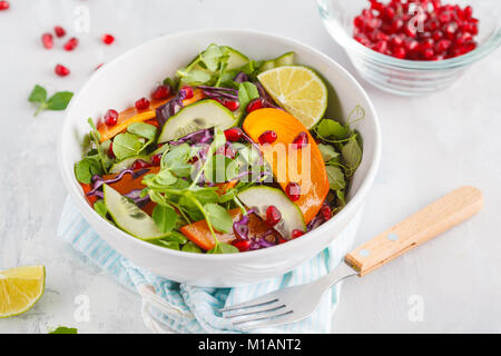 Persimmon insalata con foglie di piselli, cetriolo e melograno. Una sana alimentazione vegetariana concetto. Foto Stock